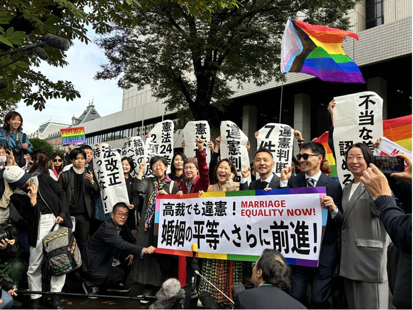 東京高裁の正門前にて「高裁でも違憲！婚姻の平等へさらに前進！」と書いた横断幕を掲げる「結婚の自由をすべての人に」東京１次原告(控訴人)と弁護団や支援者達と、それを取り囲む大勢の報道陣の様子の写真